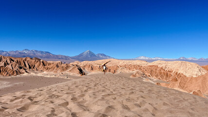 Sporty tourist woman doing handstand with wide open legs  on the top of dune in front of spectacular Licancabur volcano in Death Valley, close to San Pedro de Atacama in Chile. 