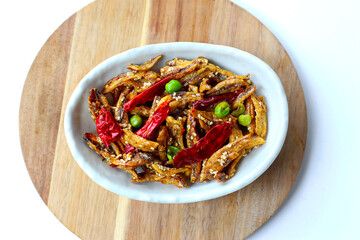 Crispy fried anchovies with sesame, dried chili, green peas, and herbs on white background.