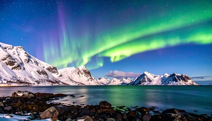 Vivid aurora borealis dances above snow-capped mountains, reflecting in calm, blue water. Rocks line foreground. Night sky