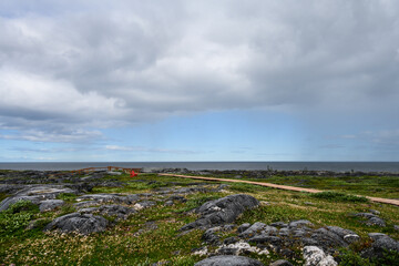 Two red Adirondack chairs in the summer tundra on the coast of Hudson Bay off the boardwalk in Cape Merry Battery park outside Churchill, Manitoba, Canada
