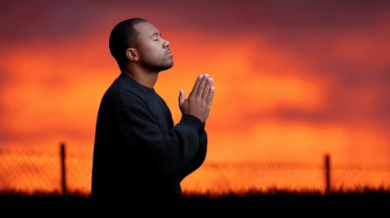 Thoughtful Man in Prayer Against a Vibrant Sunset Background with Warm Colors and Atmospheric Clouds