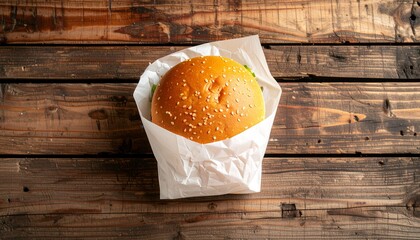 Delicious classic hamburger with a sesame seed bun, wrapped in white paper and placed on a rustic wooden table, viewed from above