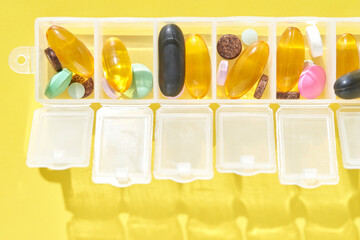 Weekly pill organizer with various supplements on bright yellow background.