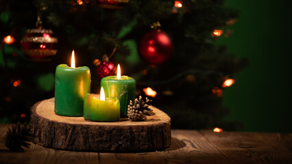 Three vibrant green candles glow softly, casting warm light on a wooden surface. Behind them, a decorated Christmas tree twinkles with festive ornaments, creating a cozy holiday atmosphere.