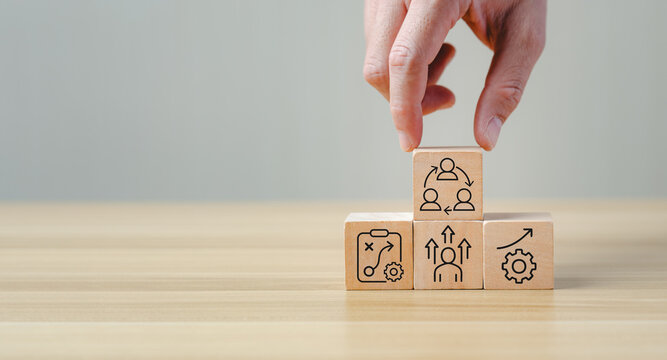 Change management process concept with hand arranging wooden blocks showing strategy, growth, learning, leadership, and teamwork icons, symbolizing organizational transformation, business improvement