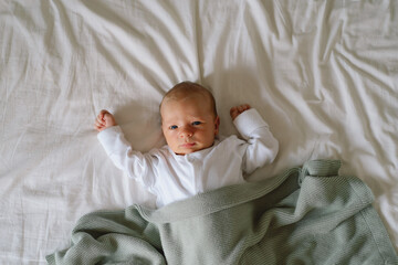 Newborn baby lying on bed under a soft blanket, capturing a moment of innocence and curiosity...