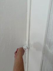 Hand painting wall corner near ceiling molding with brush. Home renovation, precise finishing work and DIY interior improvement