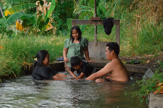 The boy carefully gauges the height of his parentsâ€™ linked hands in the stream, preparing for another attempt as his sister stands watching with interest.