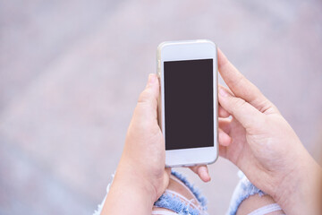 Female teen caucasian hands holding smartphone with blank screen outdoors in casual setting.