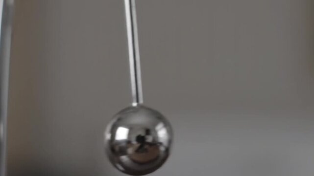 A close up of a single silver pendulum swinging rhythmically against a grey background