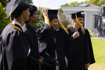 Graduating students adjusting caps and smiling joyfully while celebrating outdoors