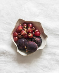 Fresh seasonal fruits grapes and figs in a ceramic bowl on a light background, top view