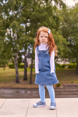 Obraz premium Young caucasian redhead girl in denim dress and blue tights outdoors in park.