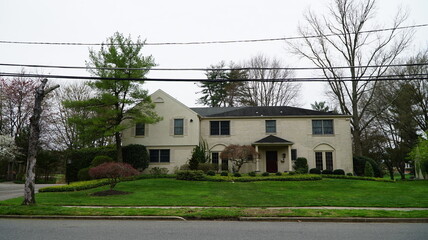 Obraz premium Front view of suburban two-story light brick house with landscaped yard and wide lawn
