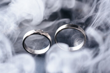 Two golden wedding rings with white smoke around, copy space and black background