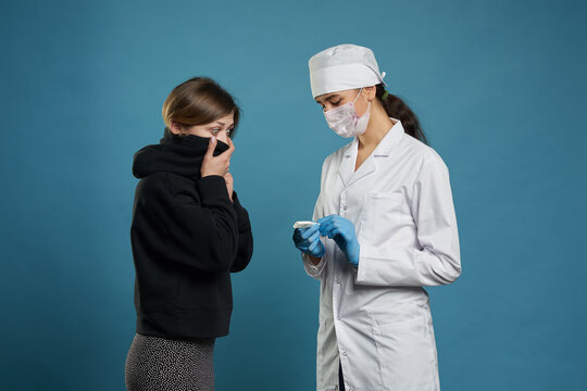 Young doctor measuring temperature of a patient with thermometer, studio shot on blue background