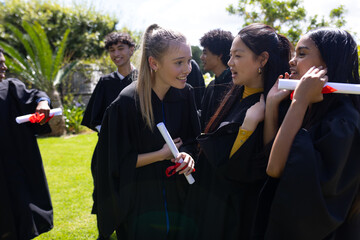Celebrating outdoors, teens in graduation gowns holding diplomas, smiling joyfully