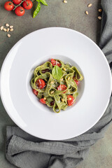 Homemade green tagliatelle pasta with pesto on a plate on the table. Italian cuisine. Top view