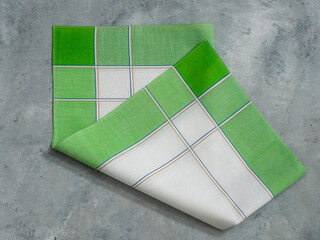 A folded vintage men's handkerchief with plaid pattern on a textured gray background.