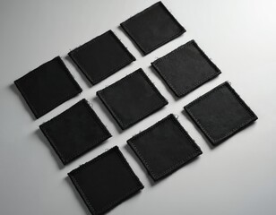 Nine identical black square textile patches neatly arranged in grid formation on white surface. Patch features blank, customizable surface with stitched edges, suitable for tactical gear uniform