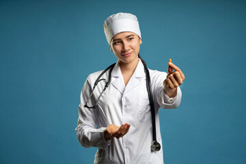Naklejka premium Young female doctor holding a pill, looking at it and giving it as a treatment to the patient