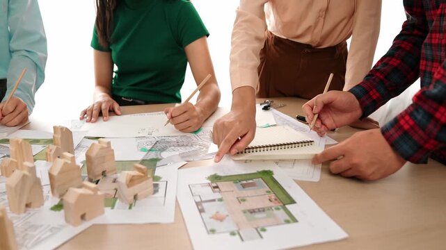Smart architect and safety engineer discussion about building blueprint on table with architectural document, measurement tools and wooden block scatter around at modern office. Closeup. Delineation.