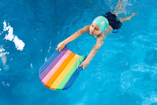 Swimming class. Close up of kids practicing flutter kick with kick board in swimming pool