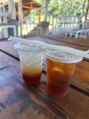 Sweet and fresh iced tea, in a plastic hood container, on a wooden table, menu in a cafe with open views of nature.