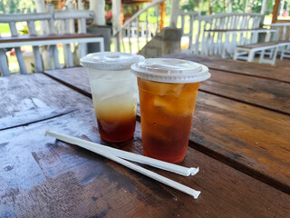 Sweet and fresh iced tea, in a plastic hood container, on a wooden table, menu in a cafe with open views of nature.