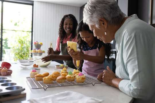 Baking cupcakes, three generations decorating with icing, sharing joyful family moments - Powered by Adobe