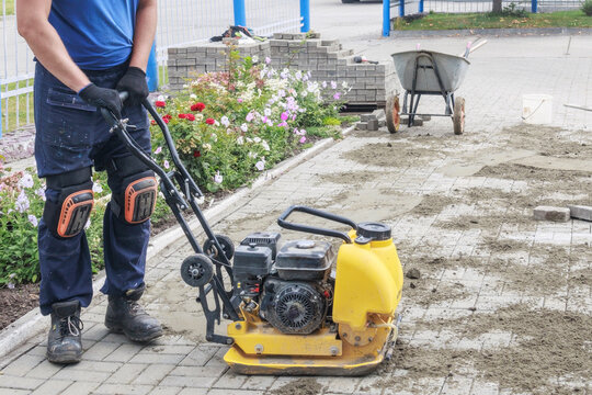 Construction Worker Operating a Plate Compactor on Paved Surface. - Powered by Adobe