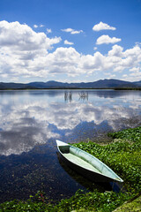 Small wooden fishing boat resting on the calm water of a lake, reflecting the beautiful cloudy sky and surrounding mountains