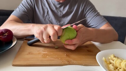 Man peeling green apple with knife, surrounded by fresh chopped fruit