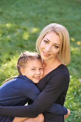 Caucasian female adult and child smiling in outdoor setting with grass background, wearing blue outfits.