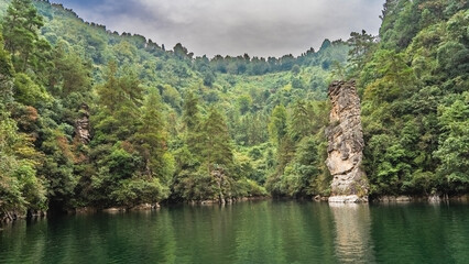 The beautiful emerald lake is surrounded by mountains. Lush green forest on the slopes. A tall pillar rock rises above the water. China. Baofeng Lake. Wulingyuan