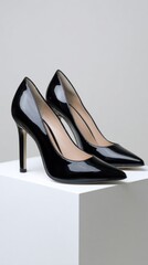 Pair of black patent leather high heels on white cube