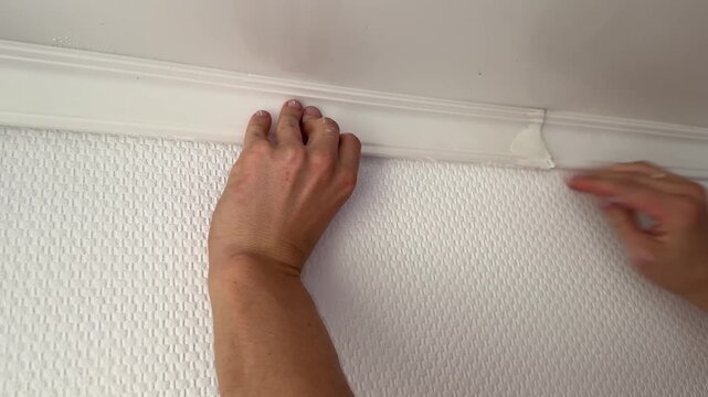 Man installing white ceiling molding at home interior. Renovation work, construction detail and household improvement