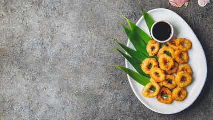 Crispy fried calamari served on a white plate with dipping sauce and green leaves