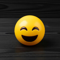 Fototapeta premium yellow emoticon rubber toy with smiling facial expression with closed eyes smiling, isolated on black wooden background