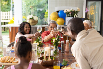 Family celebrating together outdoors, raising glasses in joyful toast at table
