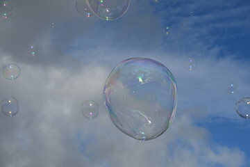 Soap bubble against a blue sky with few clouds and trees
