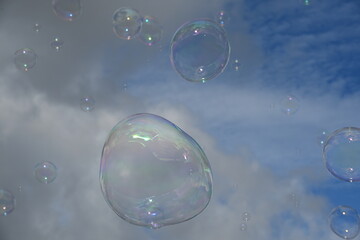 Soap bubble against a blue sky with few clouds and trees
