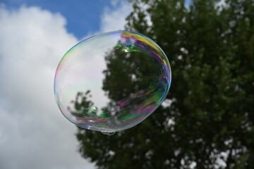 Soap bubble against a blue sky with few clouds and trees
