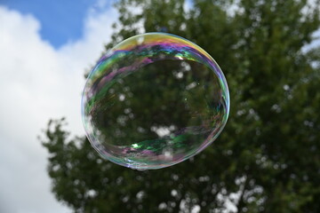 Soap bubble against a blue sky with few clouds and trees
