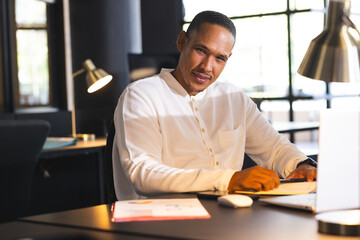 Businessman in white shirt working late at office, using laptop and smiling