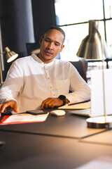 Businessman in white shirt working late at desk with documents and laptop