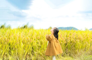 A joyful child in a brown coat gazes at the sky in a golden rice field.