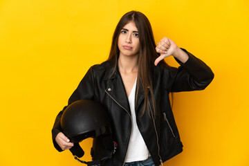 Young caucasian woman holding a motorcycle helmet isolated on yellow background showing thumb down with negative expression