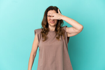 Middle aged caucasian woman isolated on blue background covering eyes by hands and smiling