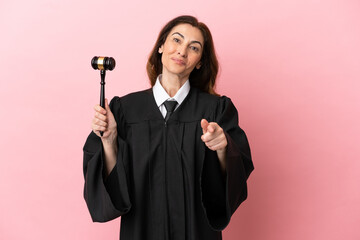 Middle aged judge woman isolated on pink background pointing front with happy expression